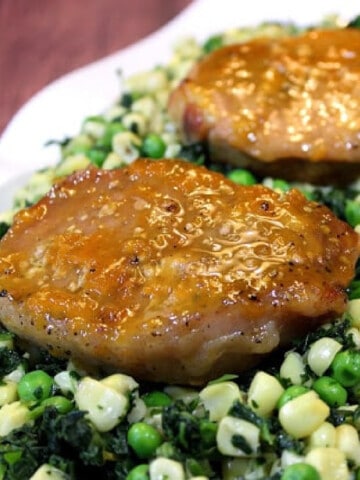 Two Apricot and Mustard Glazed Pork Chops on a bed of greens and corn.
