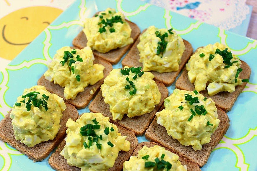 Closeup picture of egg salad on 9 squares of party bread.