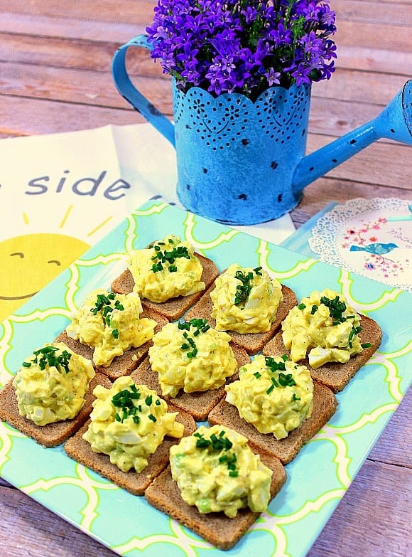 Plate of egg salad appetizers with a blue watering can and purple flowers in the background