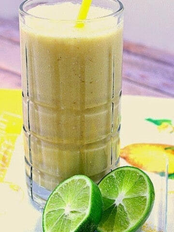 A glass of Pineapple Oatmeal Breakfast Smoothie with a cut lime in the foreground.