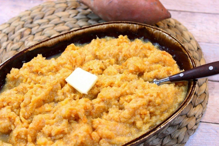 Brown bowl of cauliflower sweet potato mashers on a tan place mat.