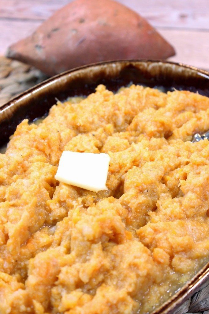 Vertical image of a bowl of mashed cauliflower and sweet potatoes and a sweet potato in the background.