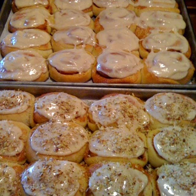 Two trays of homemade iced cinnamon rolls. One with nuts and one without.