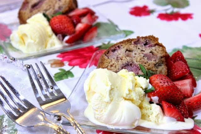 Old-Fashioned Strawberry Rhubarb Bundt Cake Two clear glass plates with cake, ice cream, and fresh strawberries on a red and green flowered tablecloth.