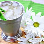 A Traditional Mint Julep in a metal cocktail glass with fresh mint and white daisies on the side.
