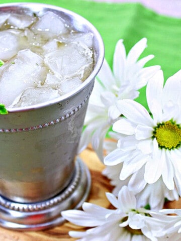 A Traditional Mint Julep in a metal cocktail glass with fresh mint and white daisies on the side.