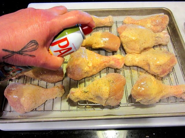 A hand spraying olive oil onto chicken legs.