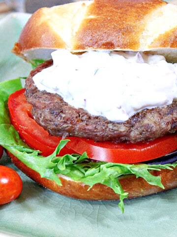 A Greek Lamb Burger with Feta and Tzatziki on a green square plate with tomato and lettuce.