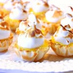 A closeup horizontal photo of a plate of Lemon Meringue Tartlets with a toasted meringue.