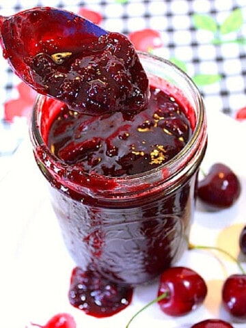 A glass mason jar and a spoon serving up some Cherry Sriracha BBQ Sauce.