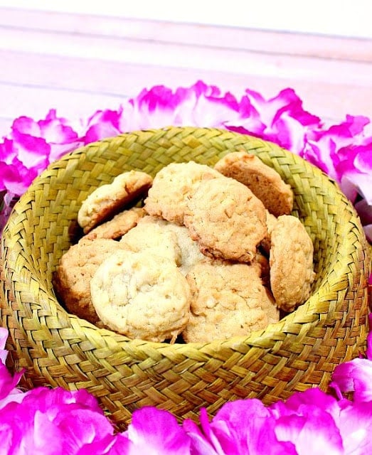 Coconut Macadamia Nut Cookies in a wicker Hawaiian hat as a bowl with pink flowers surrounding it.