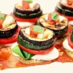 A bunch of vegetable stacks on a plate topped with sauce and basil.