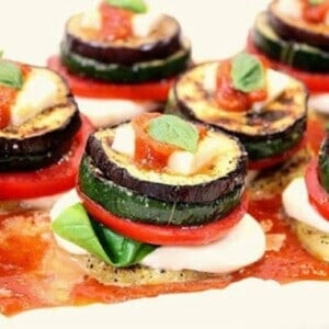 A bunch of vegetable stacks on a plate topped with sauce and basil.