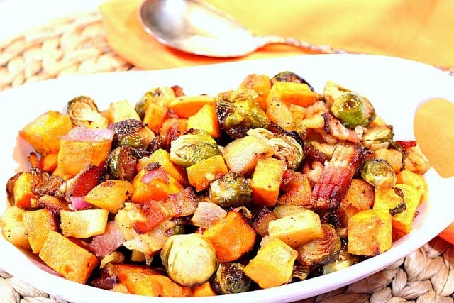 A white oval bowl filled with Roasted Sweet Potatoes with Brussels Sprouts and Apples along with bacon.