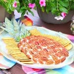 pineapple cheeseball on a platter with crackers and flowers in the background