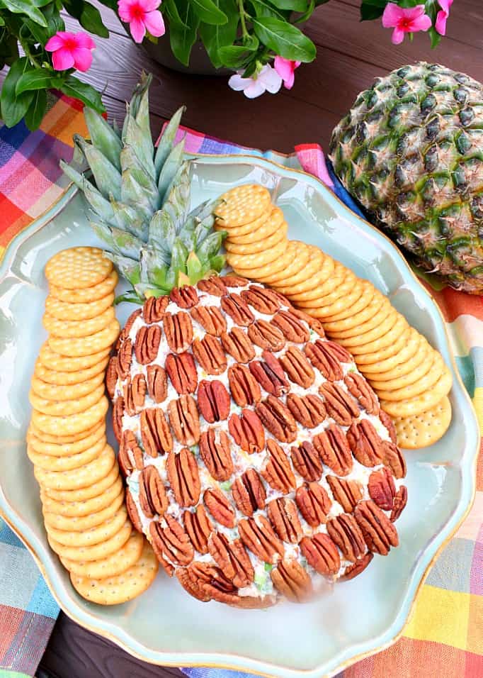 Overhead vertical photo of a pineapple cheese ball with crackers, flowers, and colorful napinks