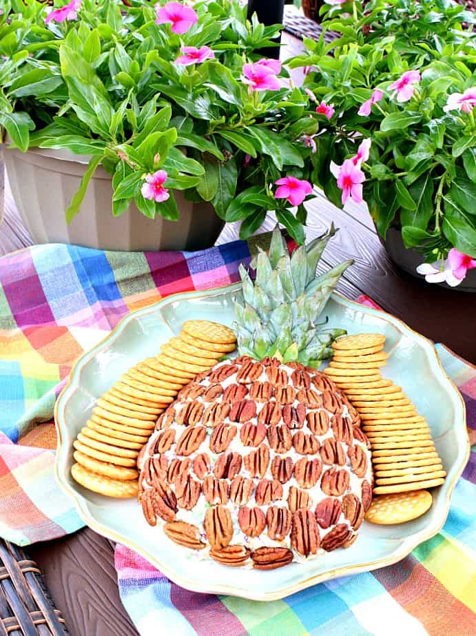Vertical image of a pineapple cheese ball on a platter with crackers and colorful napkins