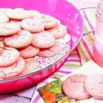 A pink tray filled with Pink Lemonade Cookies along with a glass of pink lemonade on the side.