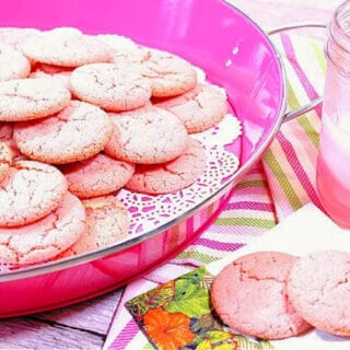 A pink tray filled with Pink Lemonade Cookies along with a glass of pink lemonade on the side.