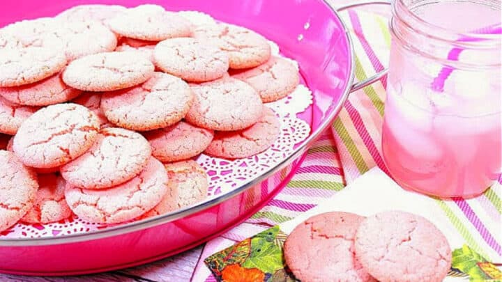A pink tray filled with Pink Lemonade Cookies along with a glass of pink lemonade on the side.