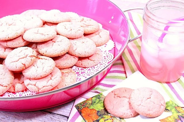 pink lemonade cookies in a pink tray with pink lemonade in a glass on the side.