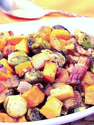 A white oval bowl filled with Roasted Sweet Potatoes with Brussels Sprouts and Apples along with bacon.