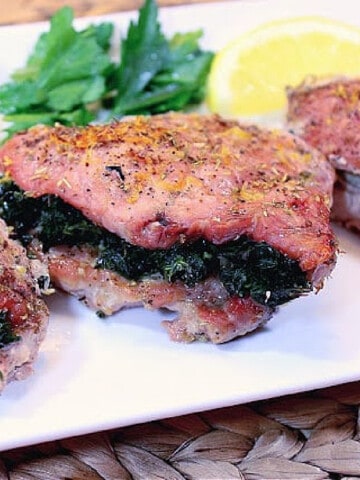 A Spinach and Feta Stuffed Pork Chop on a plate with parsley and lemon slices.