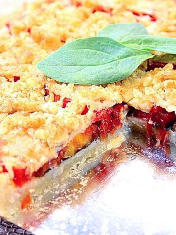 A Tomato Spinach Tart with a slice taken out and some fresh spinach leaves on top.