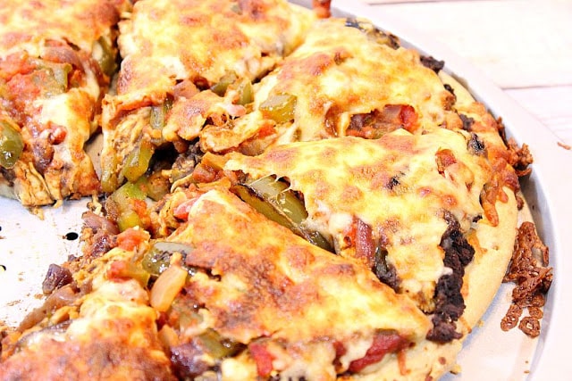 This Southwestern Chicken Fajita Pizza combines two of my favorite things; Pizza and chicken fajitas. It also comes together quickly because it utilizes store-bought pizza crust, and rotisserie chicken. - Kudos Kitchen by Renee - kudoskitchenbyrenee.com A sliced Chicken Fajita Pizza with melted cheese and green peppers.