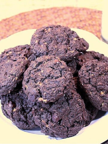 A stacked bunch of Chocolate Oat Toffee Chip Cookies on a plate with a glass of milk in the background.