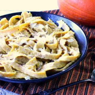 A black bowl filled with homemade pumpkin pasta with sage and a small real pumpkin in the background