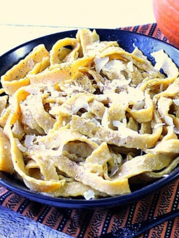 A round black bowl filled with Homemade Pumpkin Pasta with Sage topped with Parmesan.