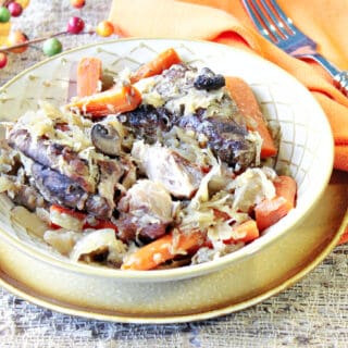 A bowlful of German Pork Ribs and Sauerkraut along with carrots, an orange napkin, and a fork.