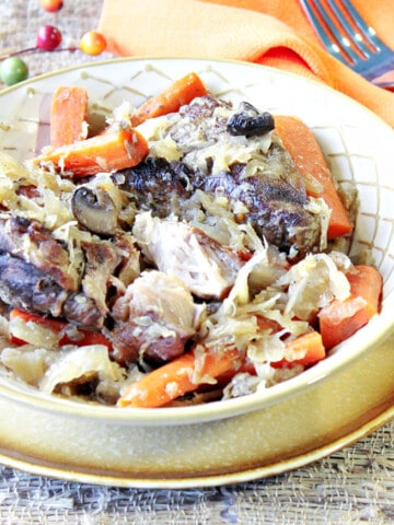 A bowlful of German Pork Ribs and Sauerkraut along with carrots, an orange napkin, and a fork.