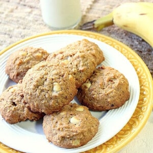 A yellow and white plate filled with Banana Walnut Cookies with a glass of milk and a banana in the background.