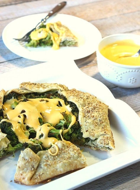 Roasted Broccoli Crostata with Cheese Sauce on a platter with a bowl of cheese sauce.