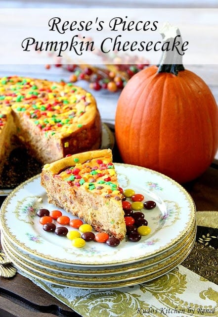 A Reese's Pieces Pumpkin cheesecake on a stack of plates with candy and a pumpkin in the background.