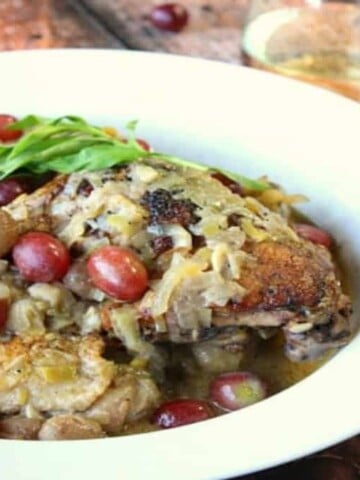 A white bowl filled with Riesling braised chicken thighs, red grapes and fresh tarragon.