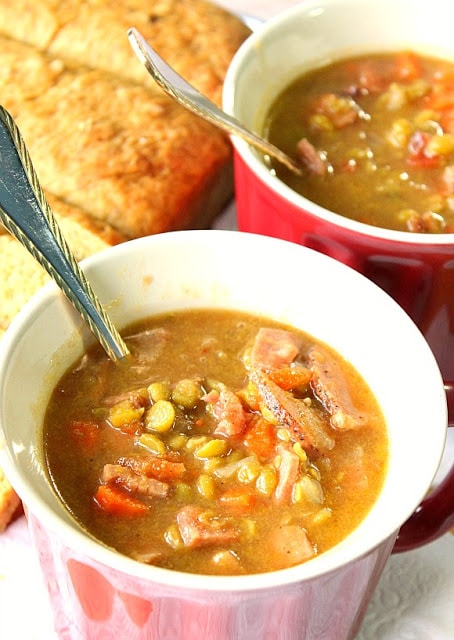 A vertical closeup photo of a mug of split pea soup with ham with a serving spoon. Comfort Food Soup, Stew, and Chowders recipe roundup.