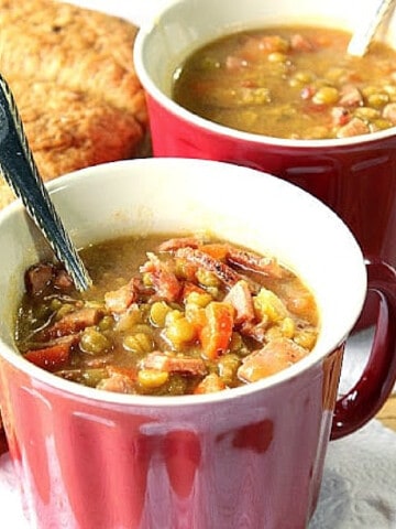 Two red mugs filled with Split Pea Soup with Ham and spoons.