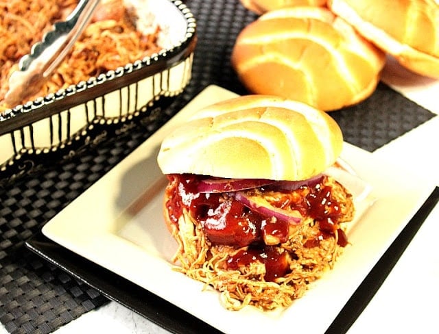 A BBQ Pulled Chicken Sandwich on a square white plate with a bun and BBQ Sauce.