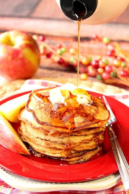 A stack of apple cider pancakes with syrup being poured down on them.