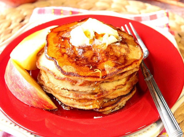 A stack of Apple Cider Pancakes with apple slices on a red plate with butter and a fork.