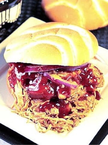 A BBQ Pulled Chicken Sandwich on a square white plate with a bun and BBQ Sauce.