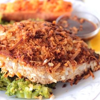 A Coconut Crusted Tuna Steak on a white plate with broccoli and a sweet potato.