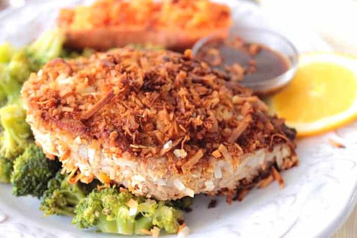 A Coconut Crusted Tuna Steak on a white plate with broccoli and a sweet potato.