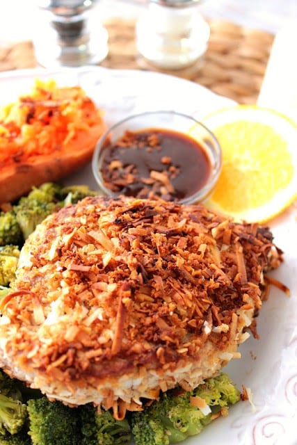 Colorful vertical image of a tuna steak crusted with coconut, a dipping sauce, sweet potato and broccoli.