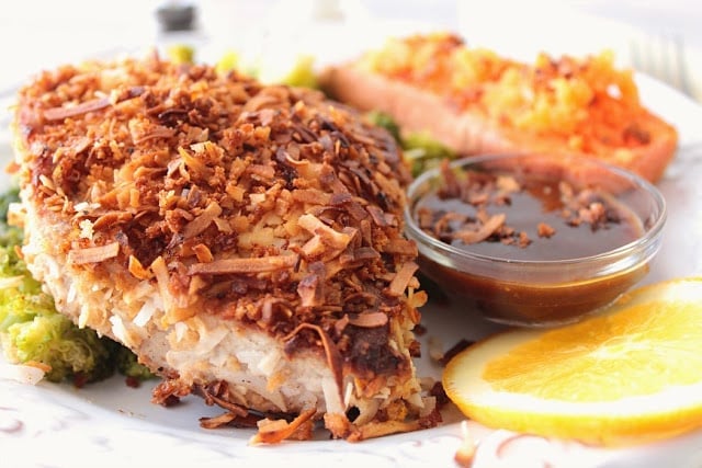Closeup picture of a coconut crusted tuna steak with dipping sauce on a white plate