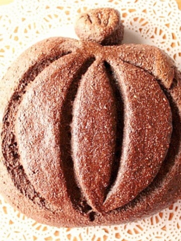 A loaf of Dark Rye Pumpkin Shaped Bread on a doily.