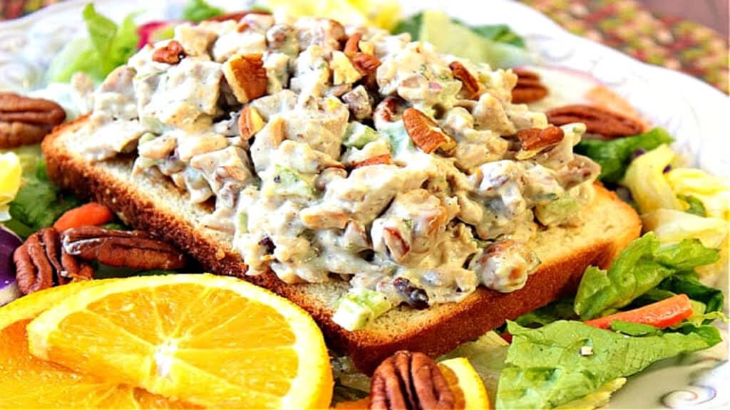 A slice of bread topped with orange cashew chicken salad with pecans and fresh oranges and lettuce.